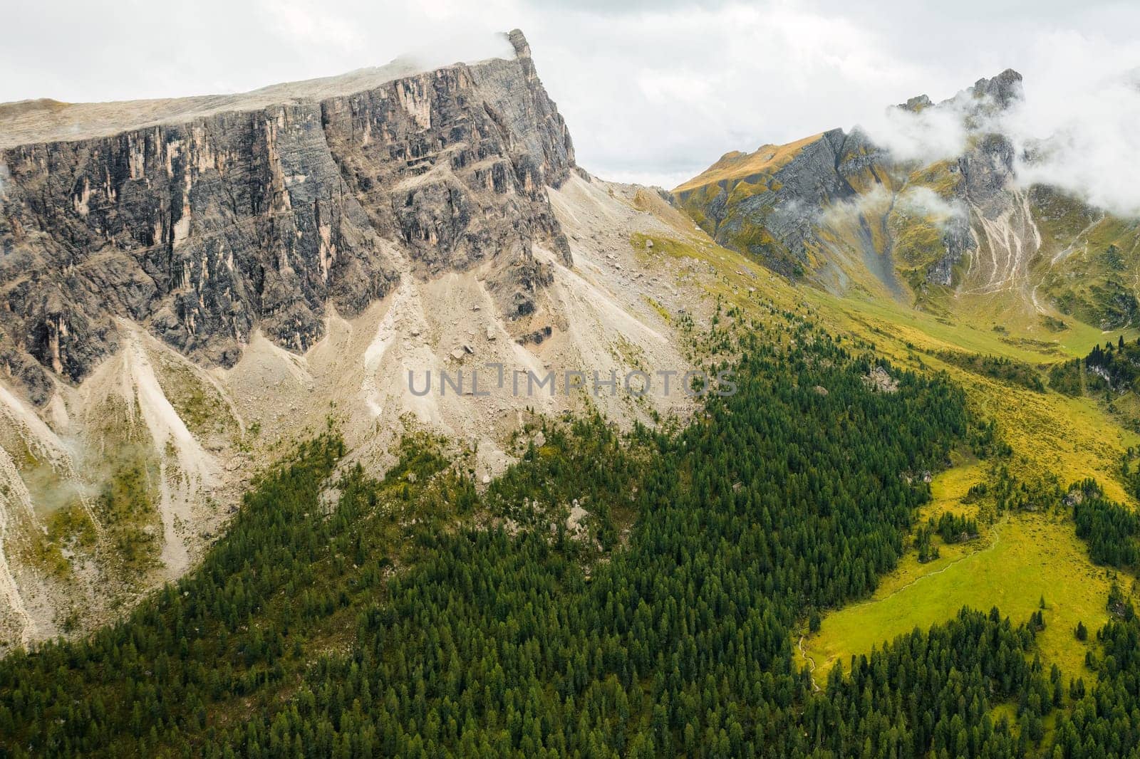 Stunning image of Rocky Dolomite Alps, where the lofty peak disappears into clouds with the forest at the mountains base.