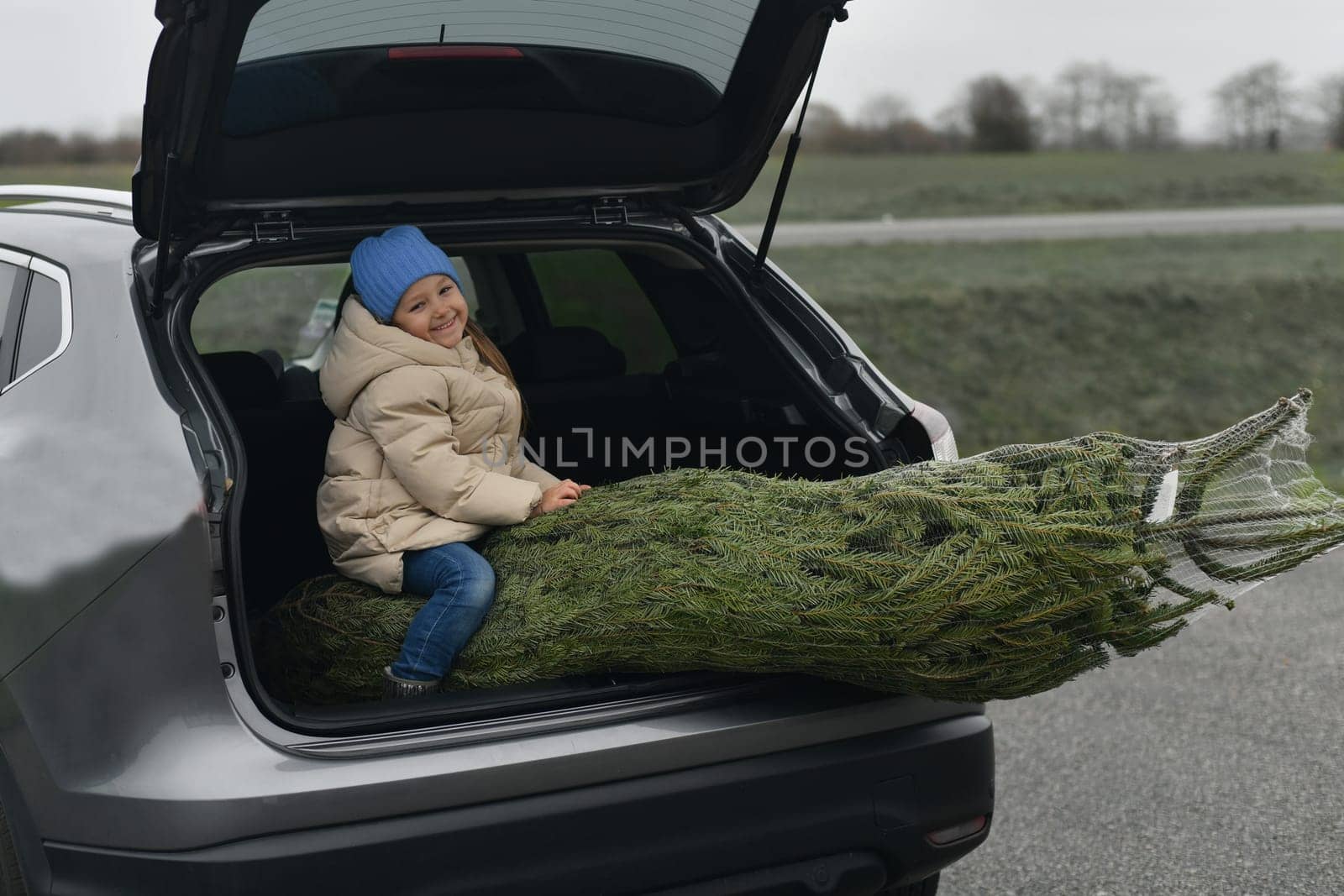 A girl sitting in the trunk with a Christmas tree