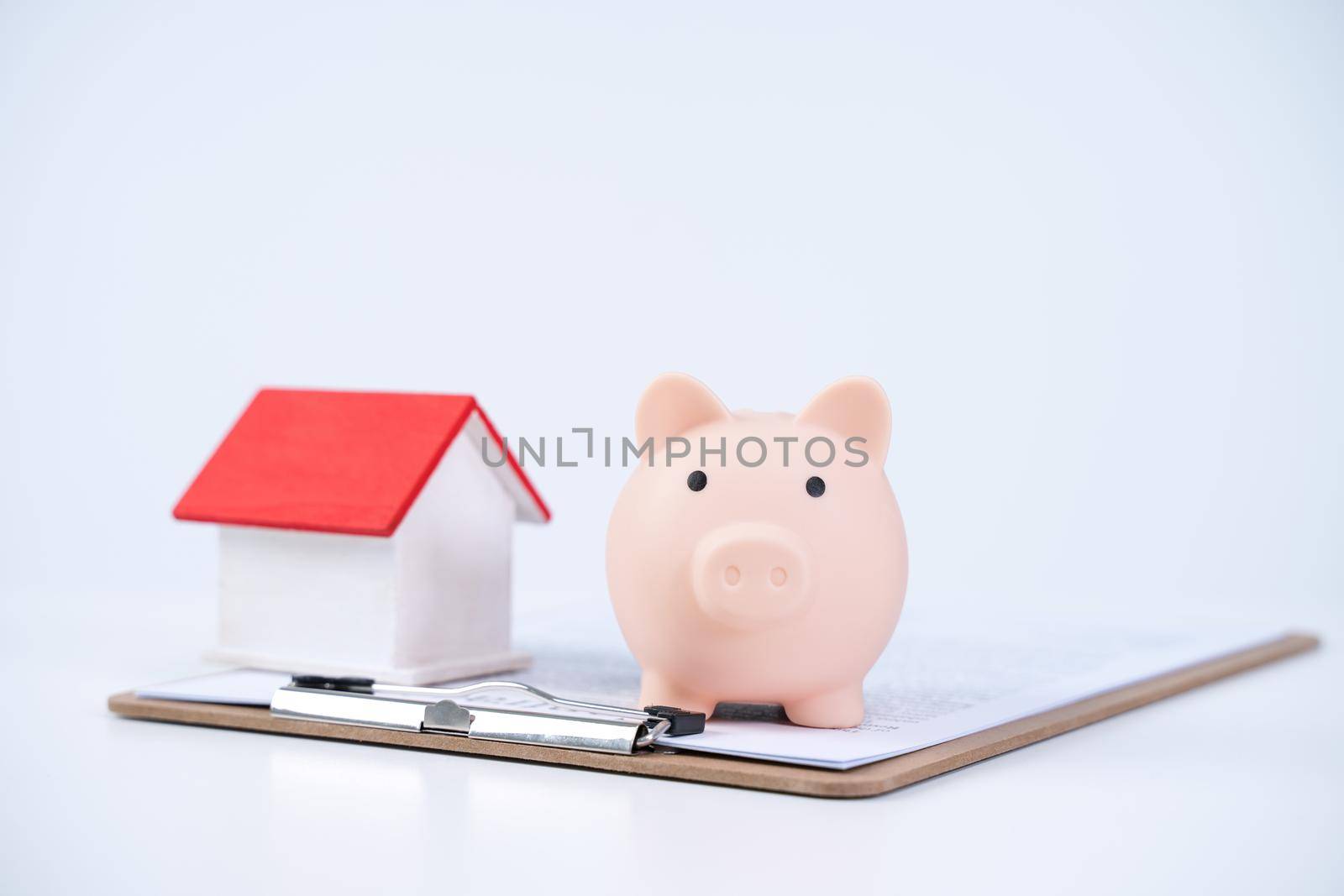 Piggy bank, beautiful wooden house model over a signed contract on white background, concept of saving money to buy a home insurance, close up, copy space.