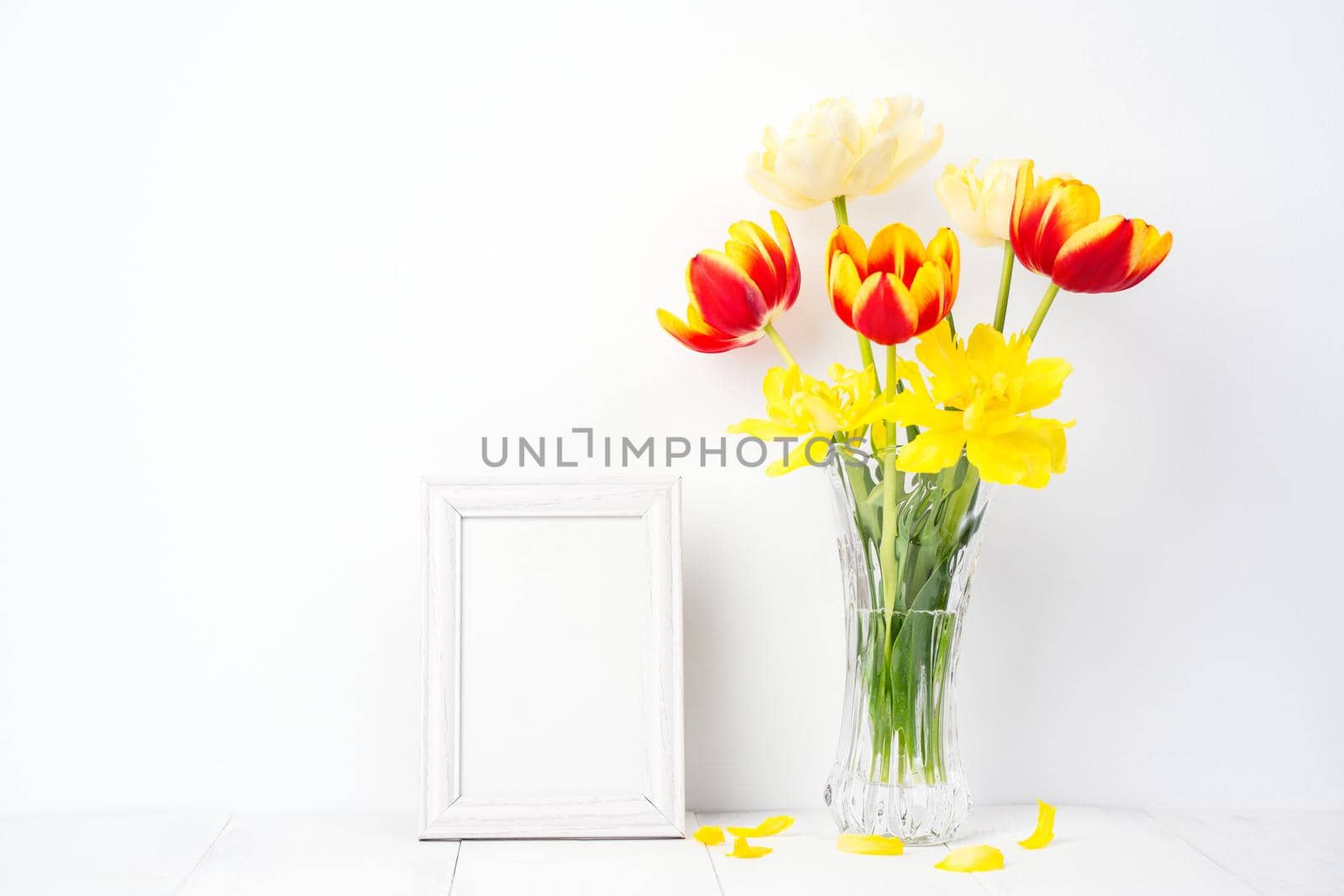 Tulip flower in glass vase with picture frame place on white wooden table background against clean wall at home, close up, Mother's Day decor concept. by ROMIXIMAGE