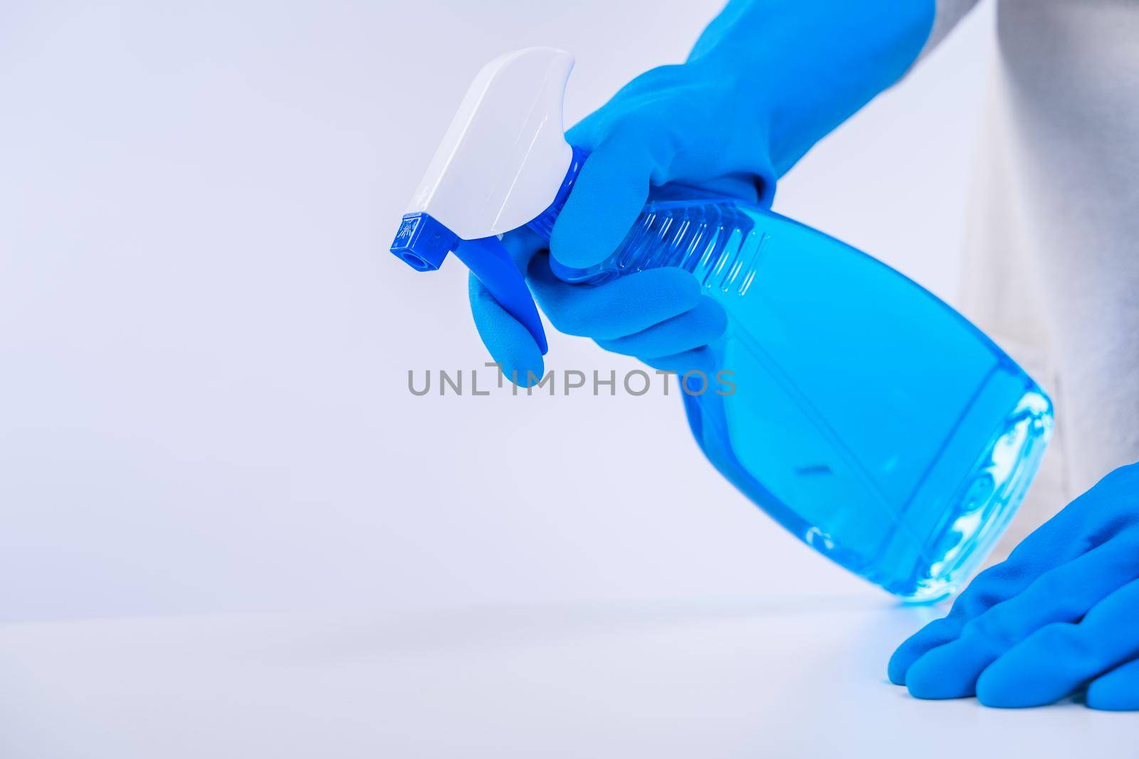 Young woman housekeeper is doing cleaning white table in apron with blue gloves, spray cleaner, wet yellow rag, close up, copy space, blank design concept.