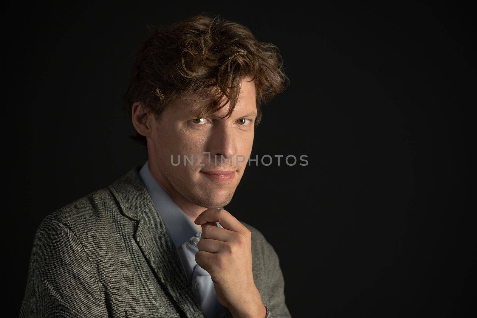 Handsome young freelancer man looking at camera with a strong look wearing suit jacket isolated on black background. Copy space on the right by LipikStockMedia