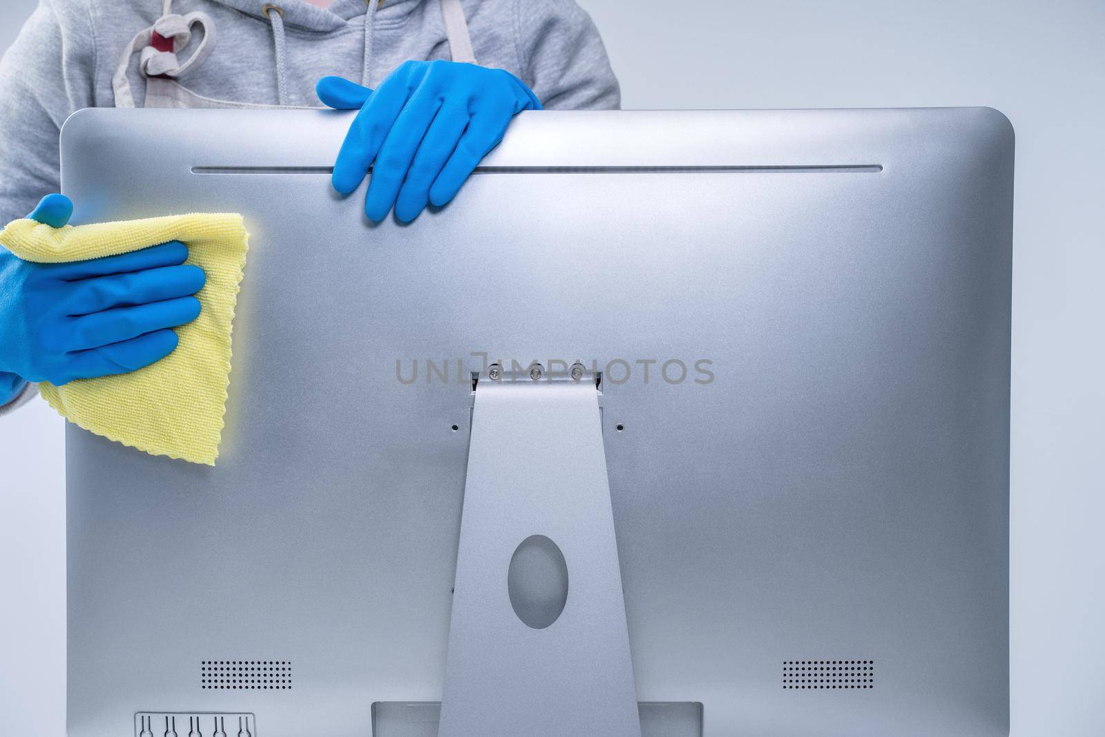 Young woman housekeeper in apron is doing cleaning silver computer screen with blue gloves, wet yellow rag, close up, copy space, blank design concept.