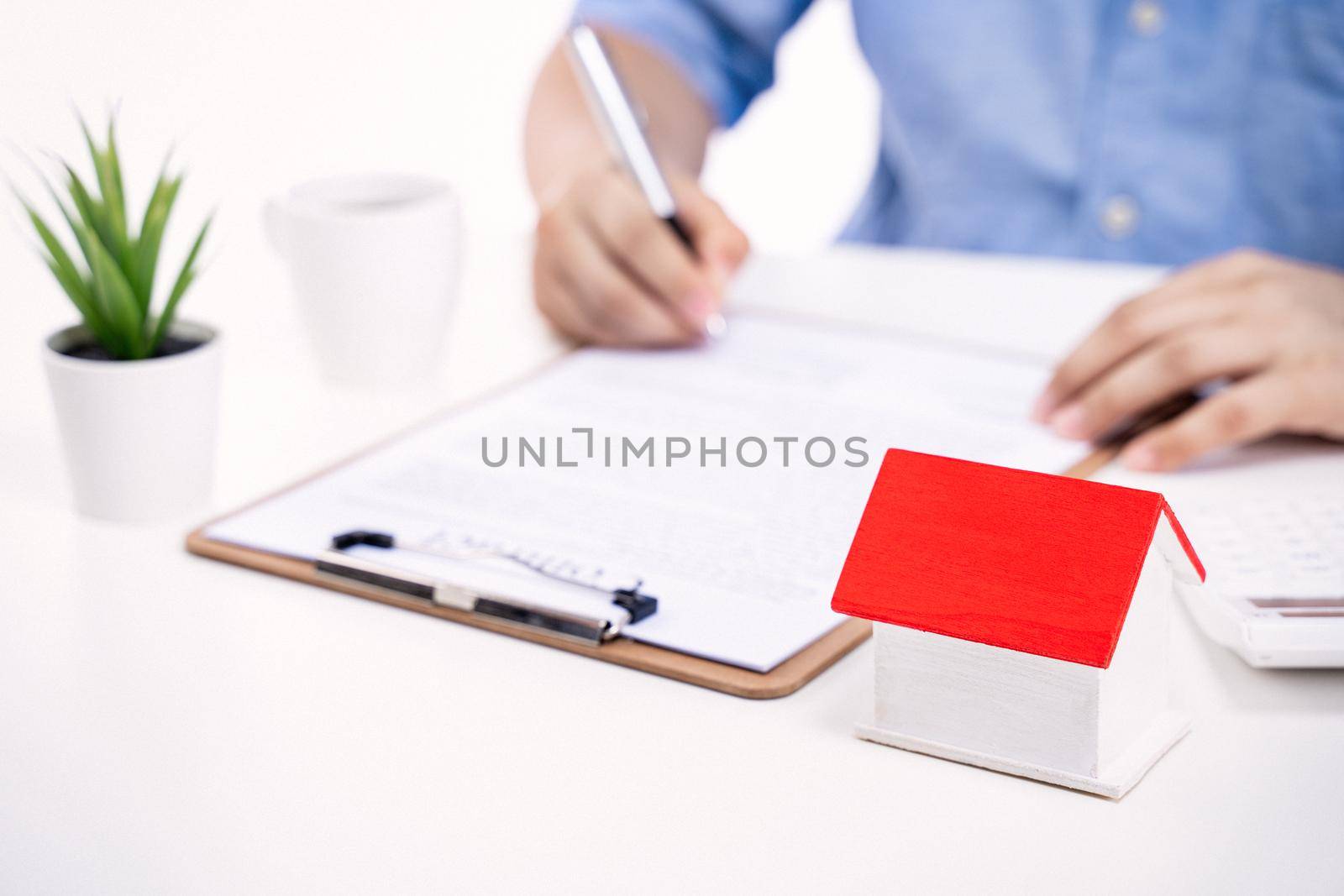 Business concept - Young Asian man in blue shirt calculates, signs agreement contract to buy a house loan payment, paying insurance, tax, close up. by ROMIXIMAGE