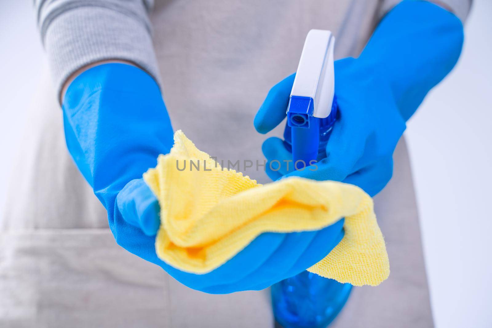 Young woman housekeeper is doing cleaning white table in apron with blue gloves, spray cleaner, wet yellow rag, close up, copy space, blank design concept. by ROMIXIMAGE