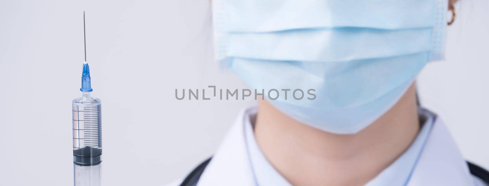 Doctor holding syringe with face mask, concept of young female physican injects coronavirus, COVID-19 vaccine on white background, close up, copy space