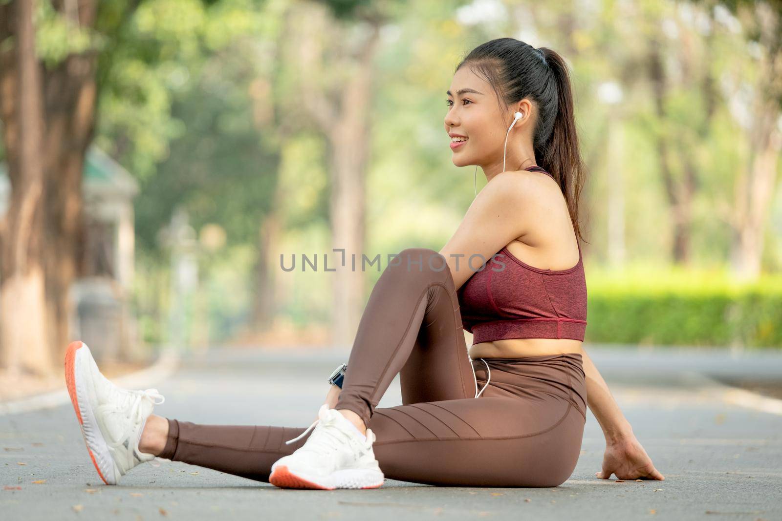 Pretty Asian woman with sportswear sit on road floor in park or garden do leg stretching and she also look to her right side.