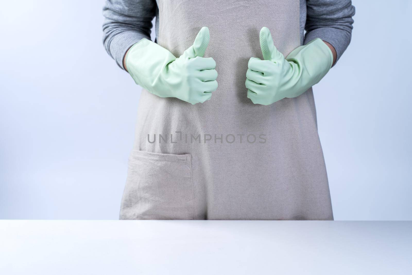 Young woman housekeeper in apron is wearing green gloves to clean the table, concept of preventing virus infection on white background, close up.