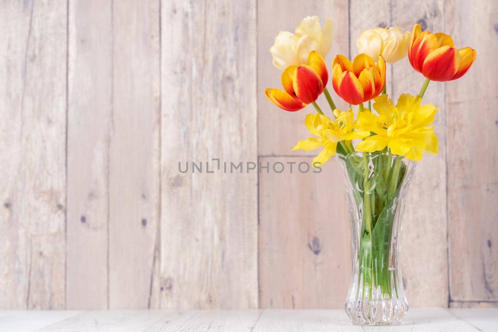 Tulip flower arrangement in glass vase with heart greeting, watering can decor on wooden table background wall, close up, Mother's Day design concept.