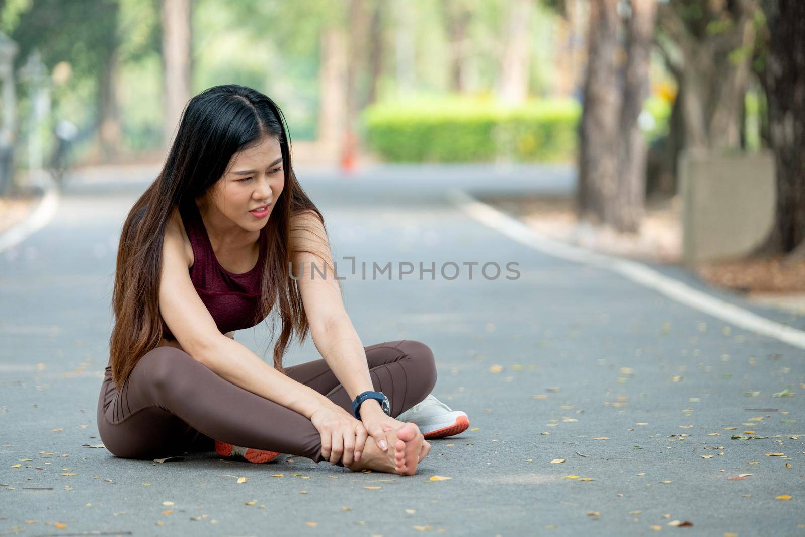Asian woman sit on road floor and hold her foot look like she got pain and injury during exercise in park or garden in the morning.