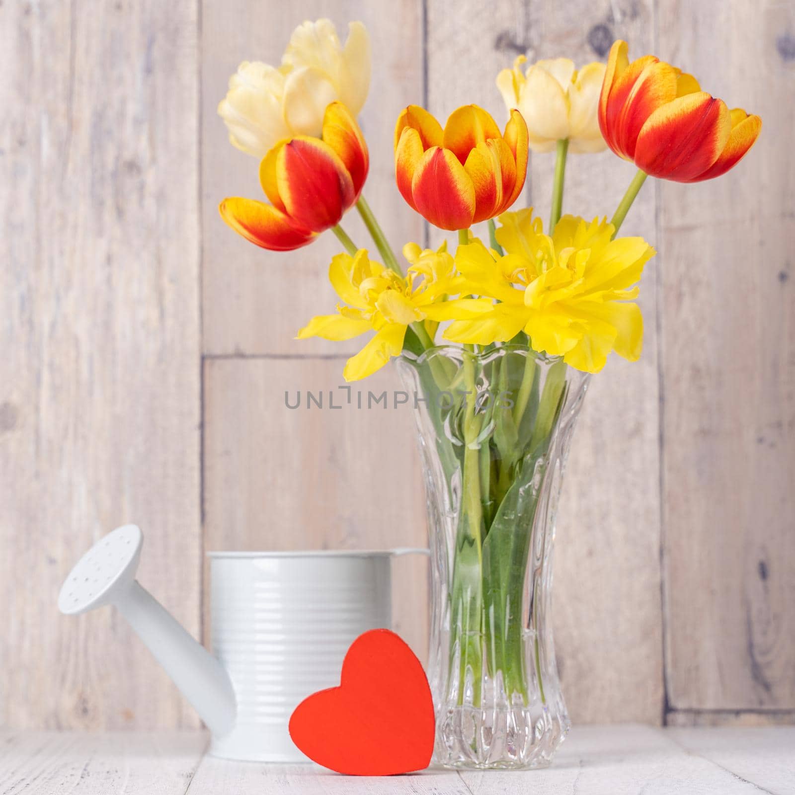 Tulip flower arrangement in glass vase with heart greeting, watering can decor on wooden table background wall, close up, Mother's Day design concept. by ROMIXIMAGE