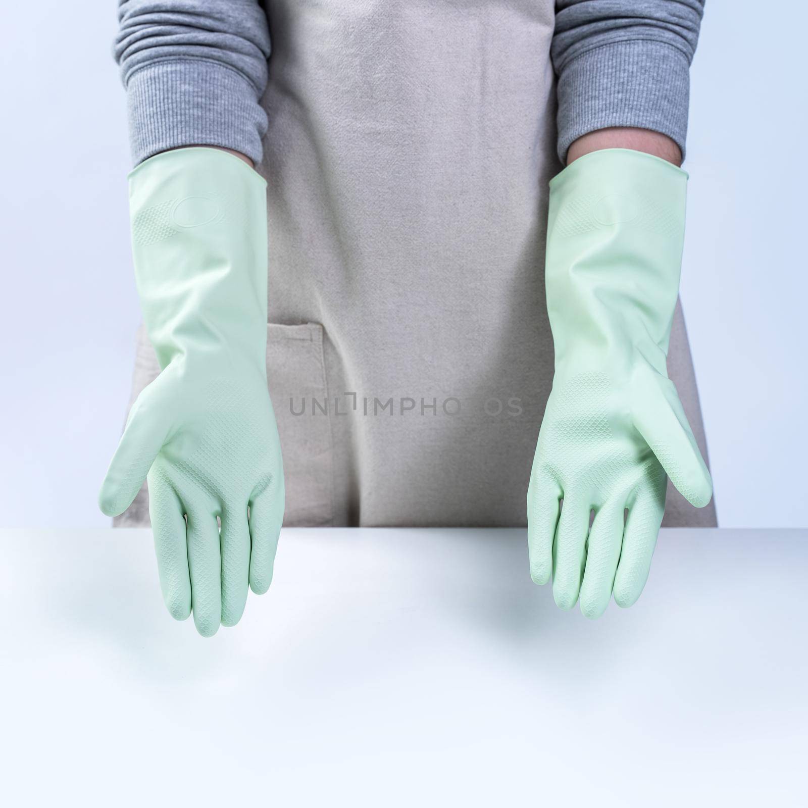 Young woman housekeeper in apron is wearing green gloves to clean the table, concept of preventing virus infection on white background, close up.