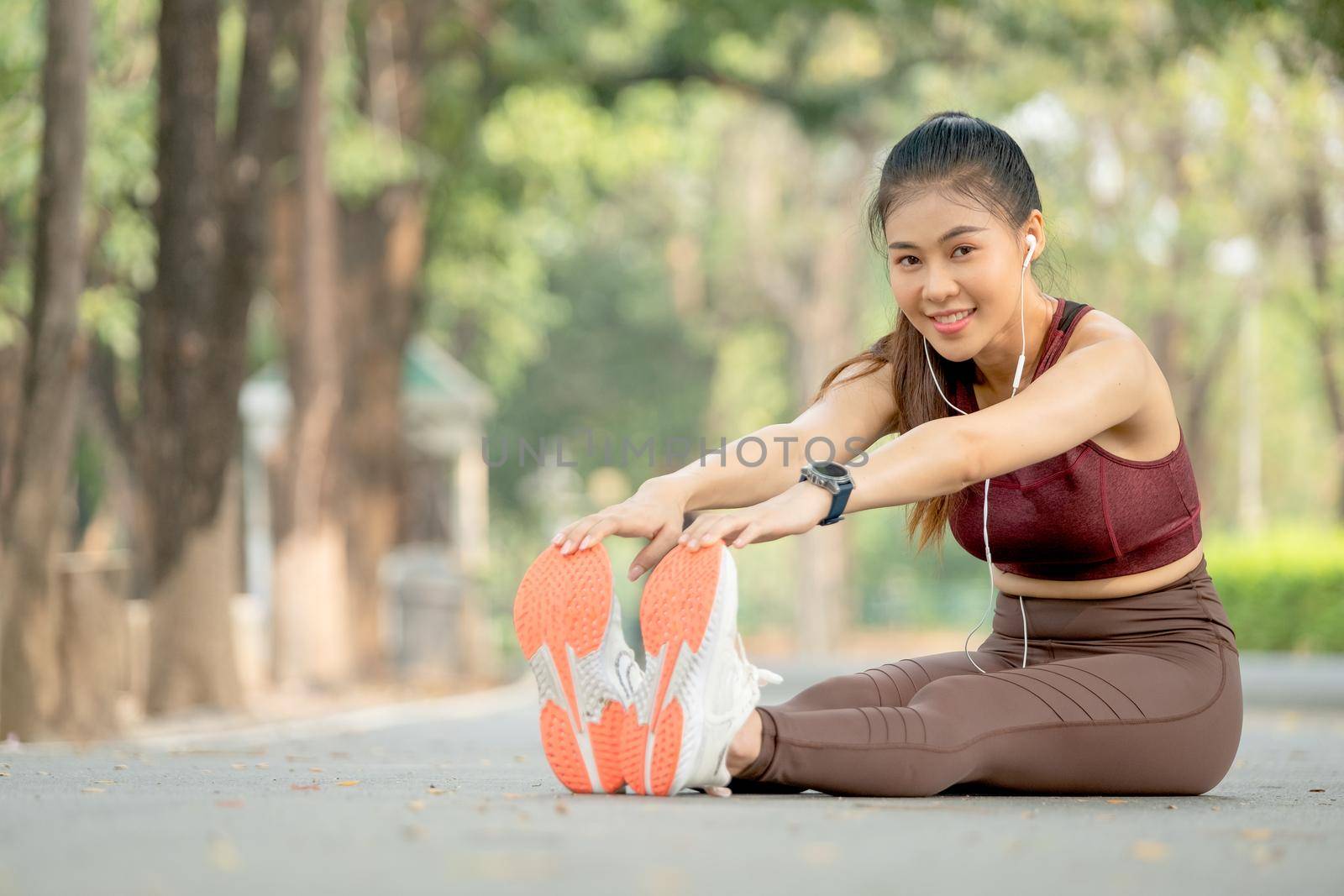 Asian beautiful sport woman with sportswear look at camera and smile during do body and legs stretching after exercise in park or garden.