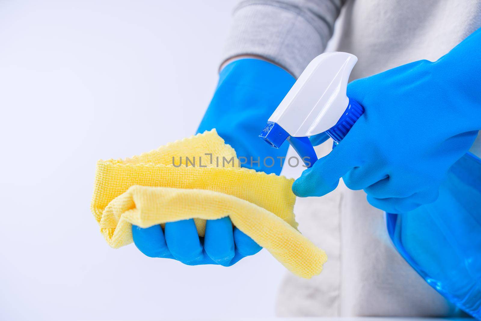 Young woman housekeeper in apron is cleaning, wiping down table surface with blue gloves, wet yellow rag, spraying bottle cleaner, closeup design concept. by ROMIXIMAGE