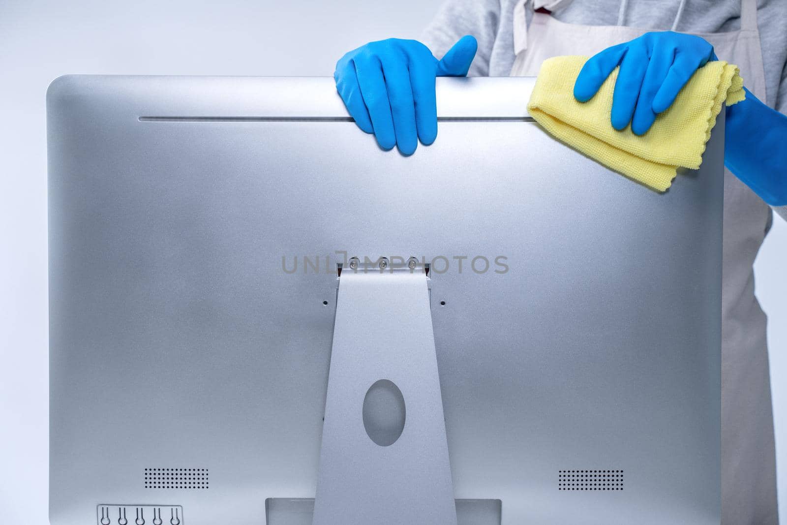 Young woman housekeeper in apron is cleaning silver computer surface with blue gloves, wet yellow rag, close up, copy space, blank design concept. by ROMIXIMAGE