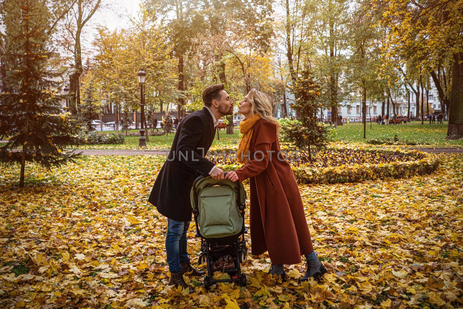 Family walking in an autumn park with a newborn baby in a stroller. Family outdoors in a golden autumn park. Tinted image by LipikStockMedia