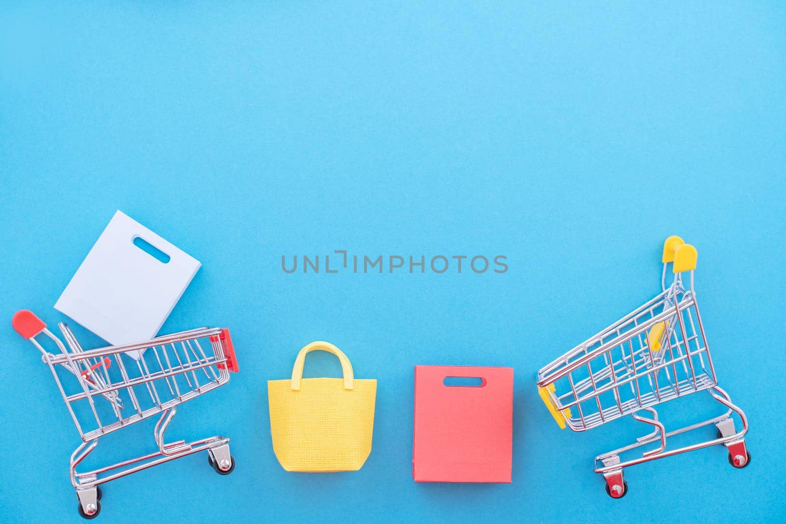 Abstract design element, annual sale, shopping season concept, mini yellow cart with colorful paper bag on pastel blue background, top view, flat lay