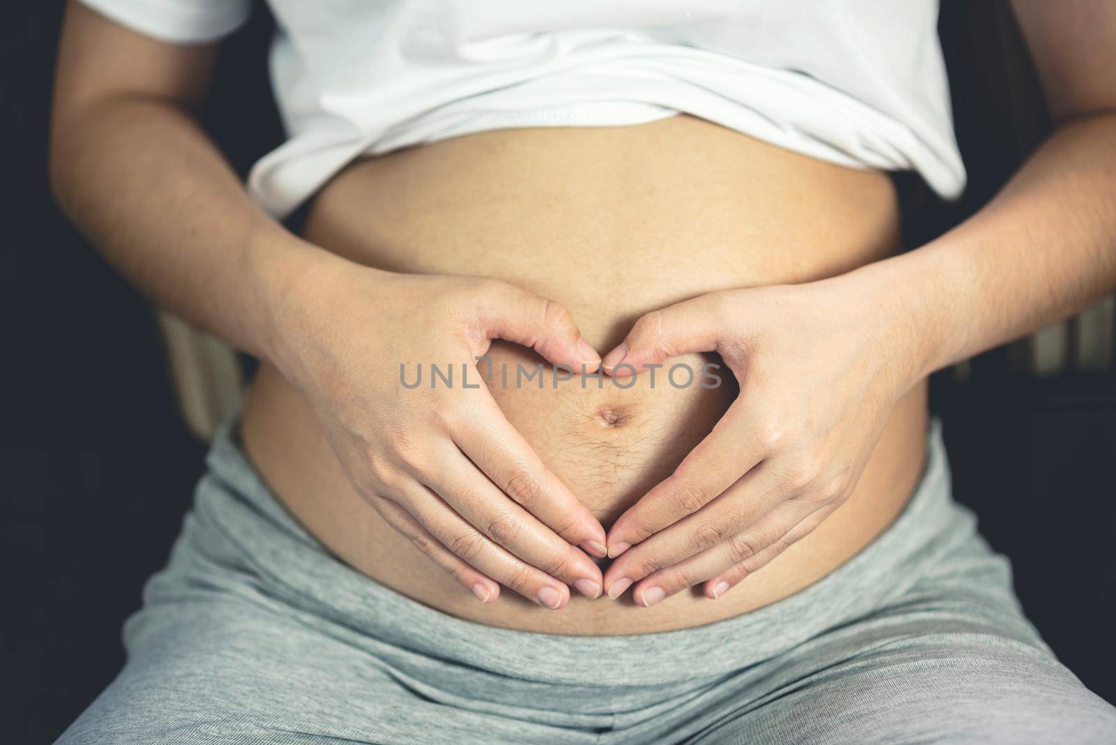 pregnant woman holding her hands on her swollen belly shaping a heart