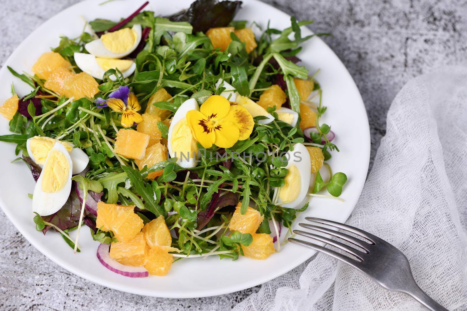 Spring fruit, citrus and vegetable salad from a mix of lettuce leaves and sprouts of radish and lentils, arugula, microgreens, quail egg wedges, with edible flowers - pansies