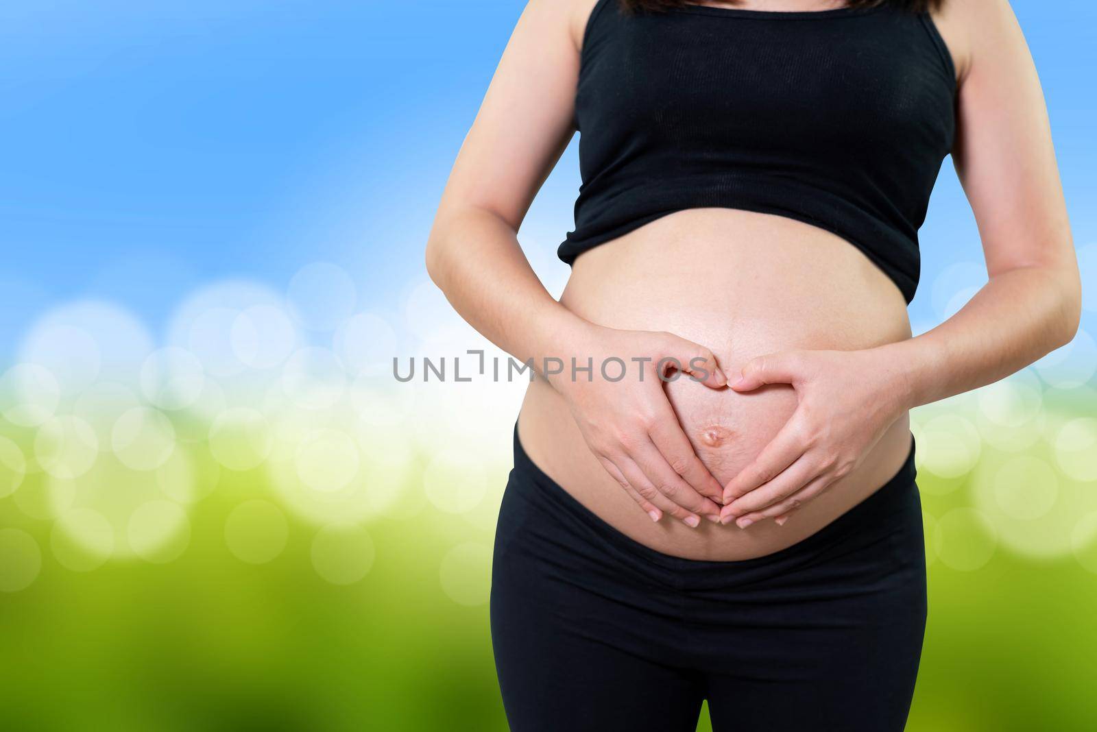 Pregnant woman holding her hands in a heart shape on her belly.