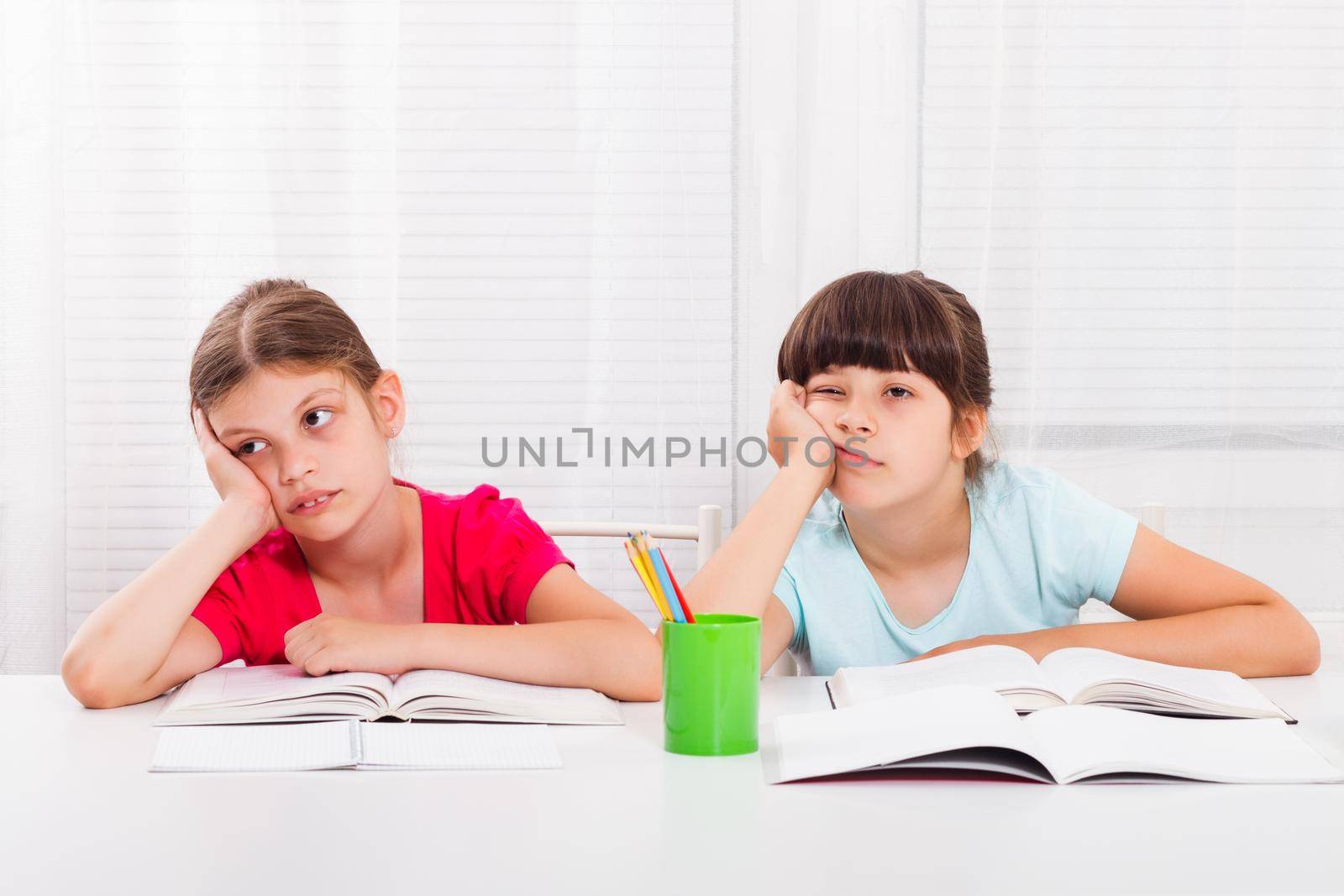 Two little bored schoolgirls sitting at table