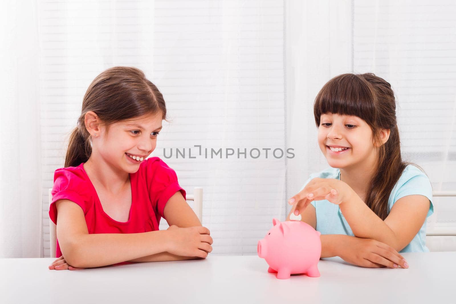 Cute little girls putting coin into piggy bank. Children's savings