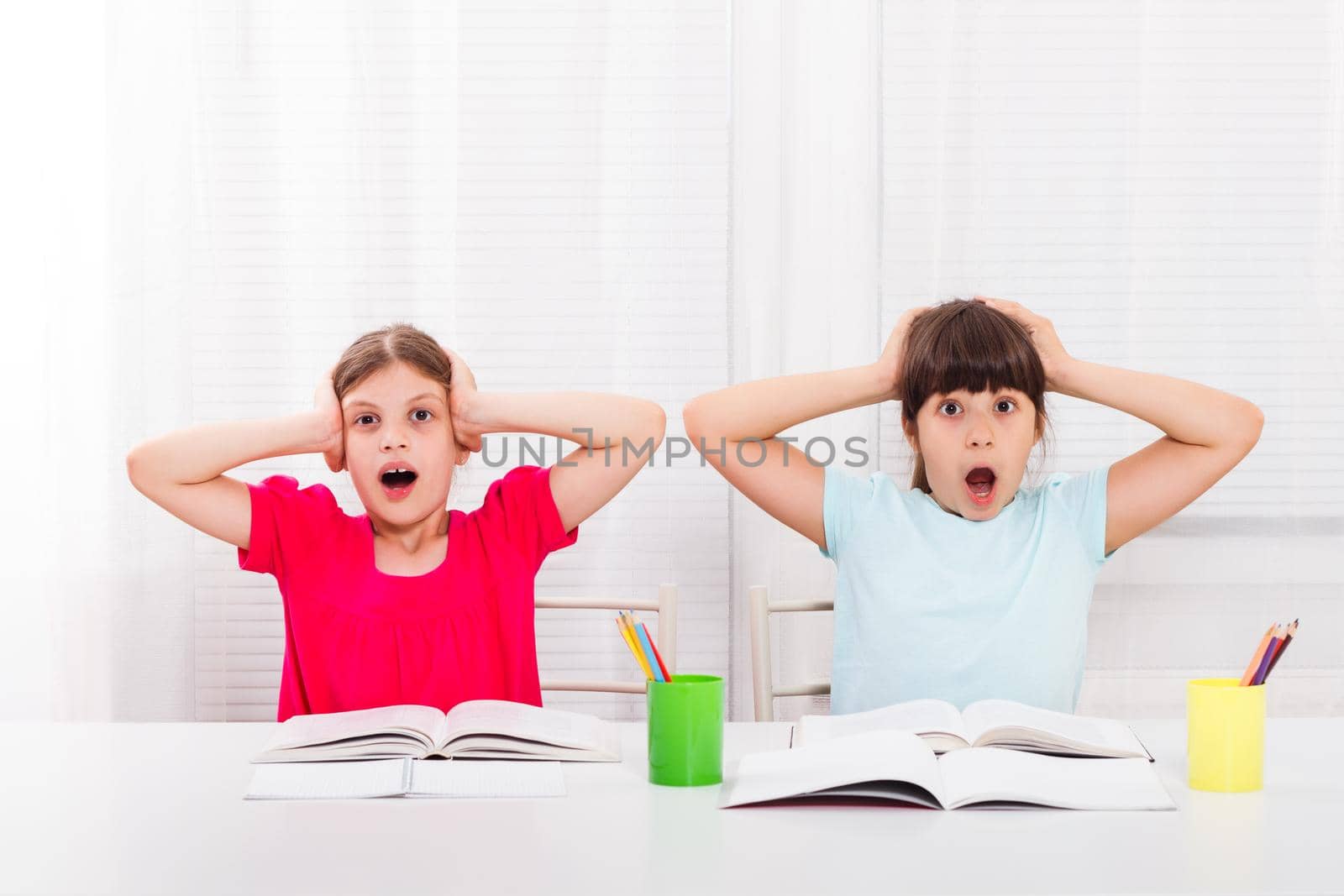 Two panicking schoolgirls with books and pencils sitting at table