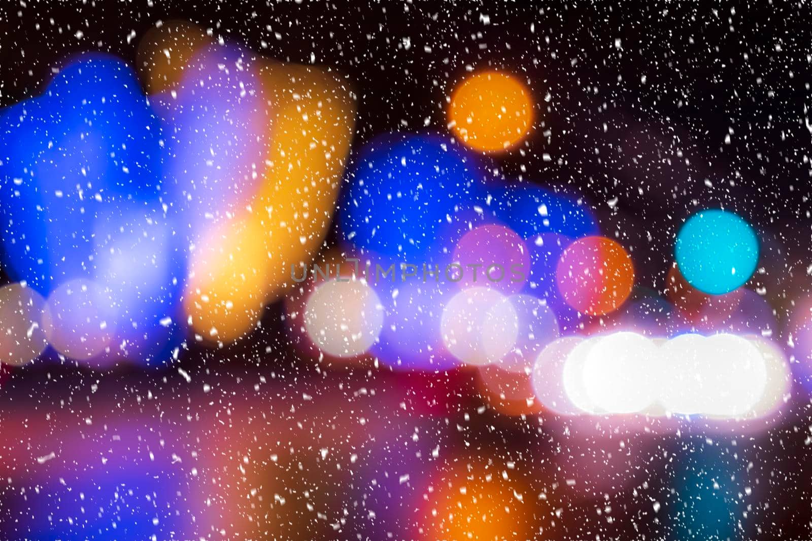 Blurred lights of headlights of cars and lanterns in the night city in a snowfall. Abstract bright bokeh.