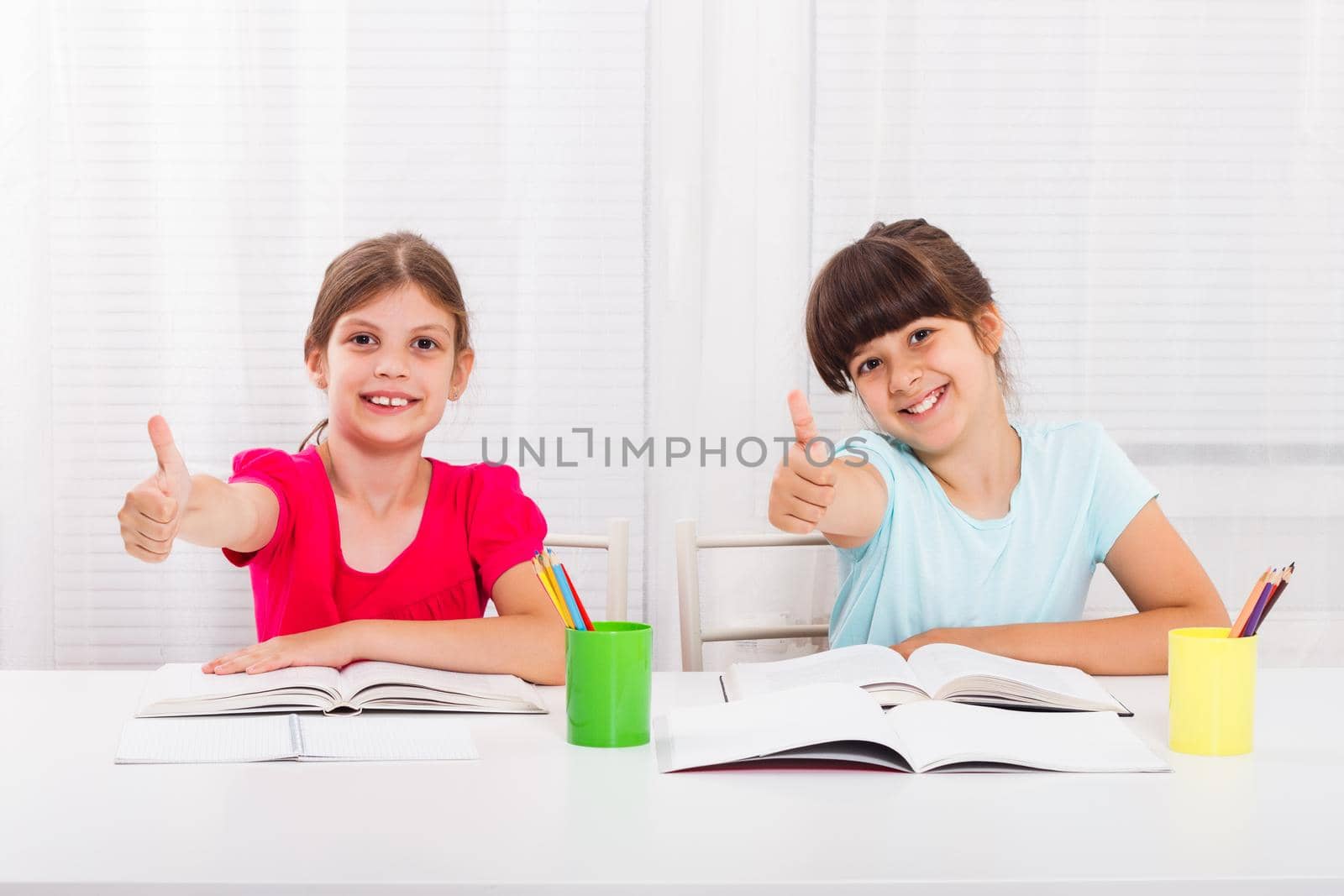 Two happy smiling schoolgirls showing thumbs up