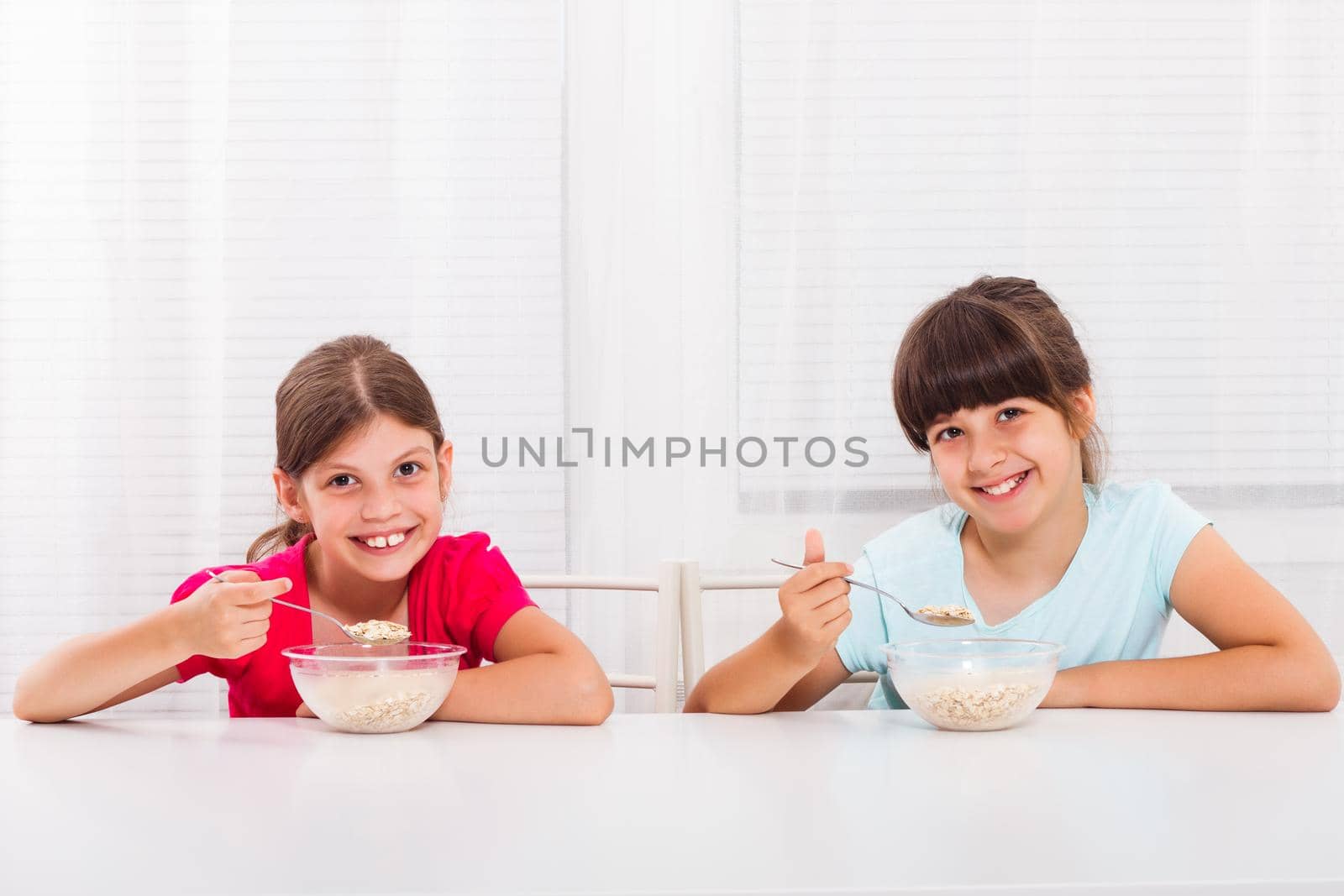 Cute little girls are sitting and eating cereals for breakfast