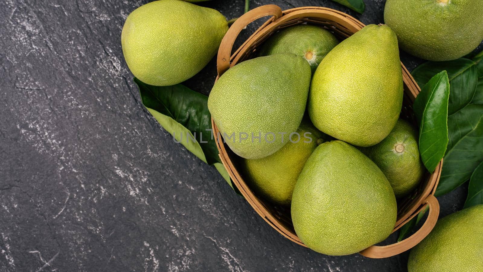 Fresh peeled pomelo, pummelo, grapefruit, shaddock on dark background in bamboo basket. Autumn seasonal fruit, top view, flat lay, tabletop shot.