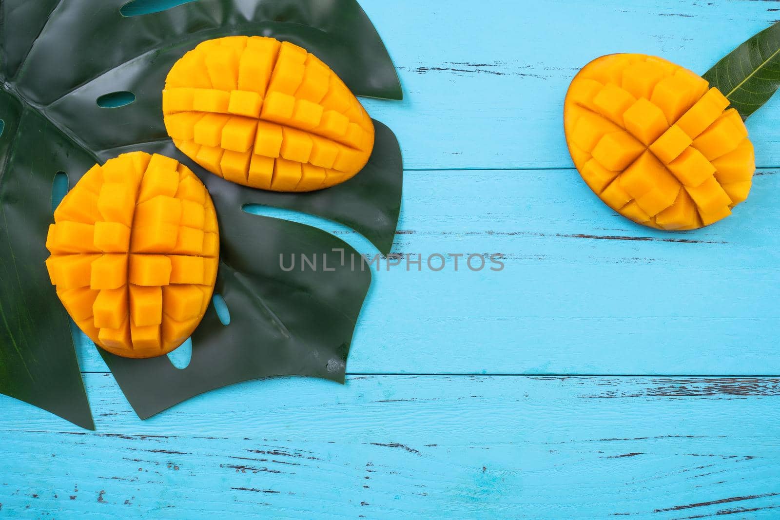 Mango - Fresh chopped tropical mango fruit isolated on bright vibrant light blue wooden table background, top view, flat lay layout, overhead shot. by ROMIXIMAGE
