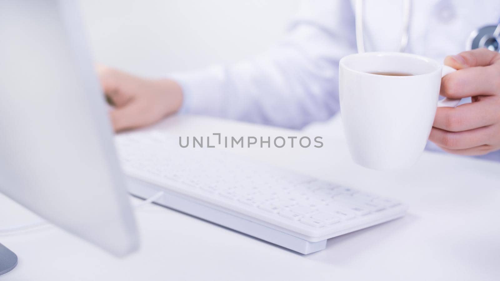 Business concept - Young female doctor woman working at office with computer, typing electronic medical record, white table background, close up, copy space by ROMIXIMAGE