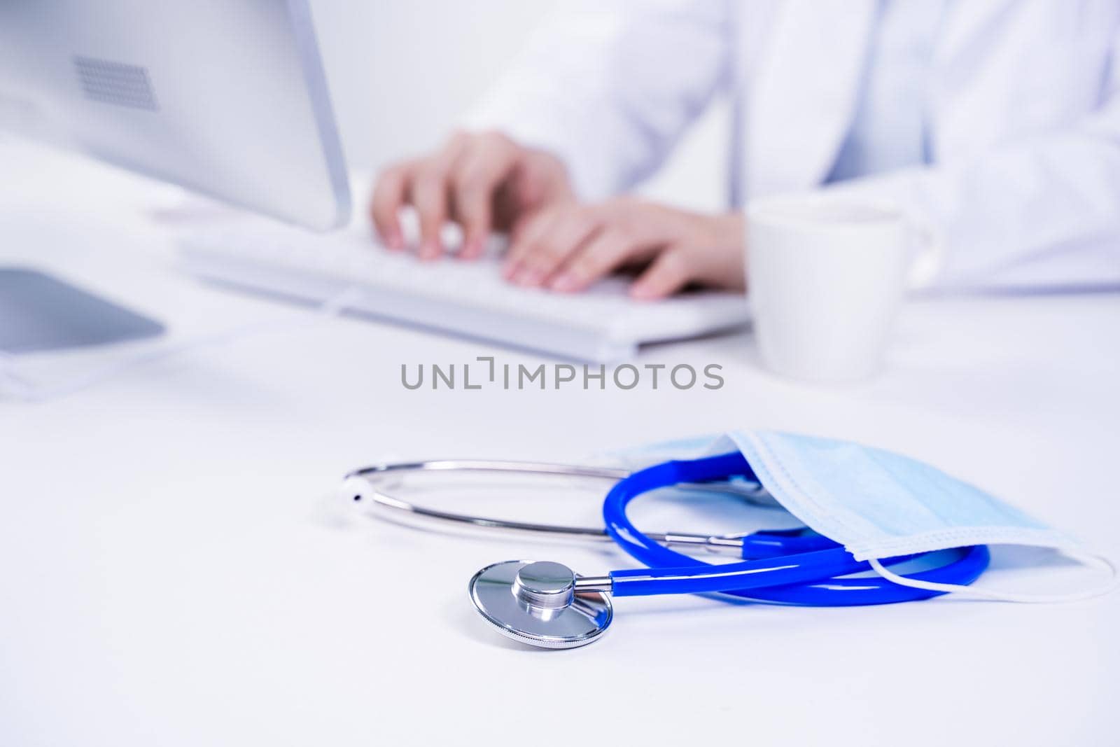 Business concept - Young female doctor woman working at office with computer, typing electronic medical record, white table background, close up, copy space by ROMIXIMAGE