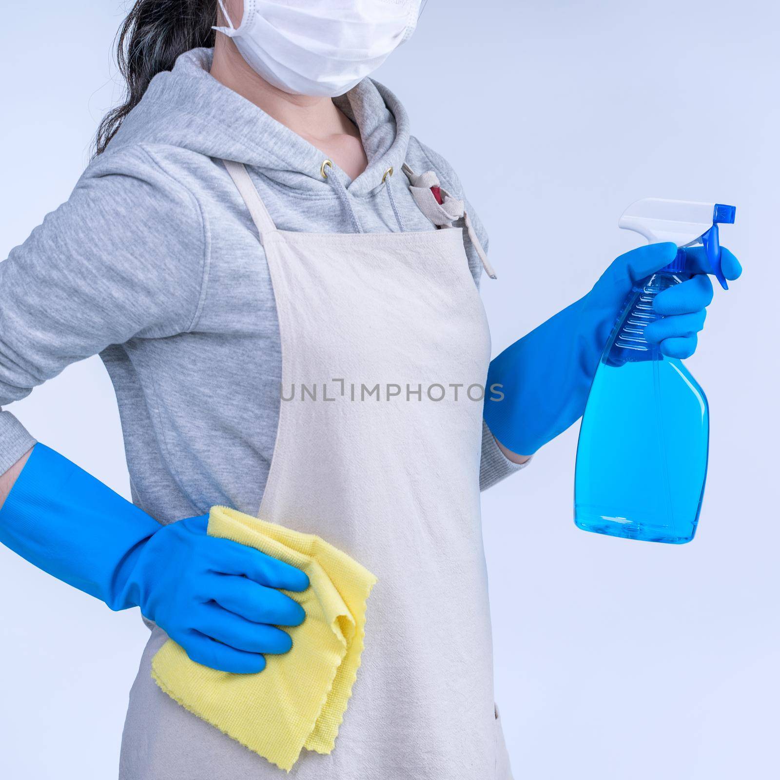 Young woman housekeeper in apron is doing cleaning with blue gloves, wet yellow rag, spraying bottle cleaner, close up, copy space, blank design concept.