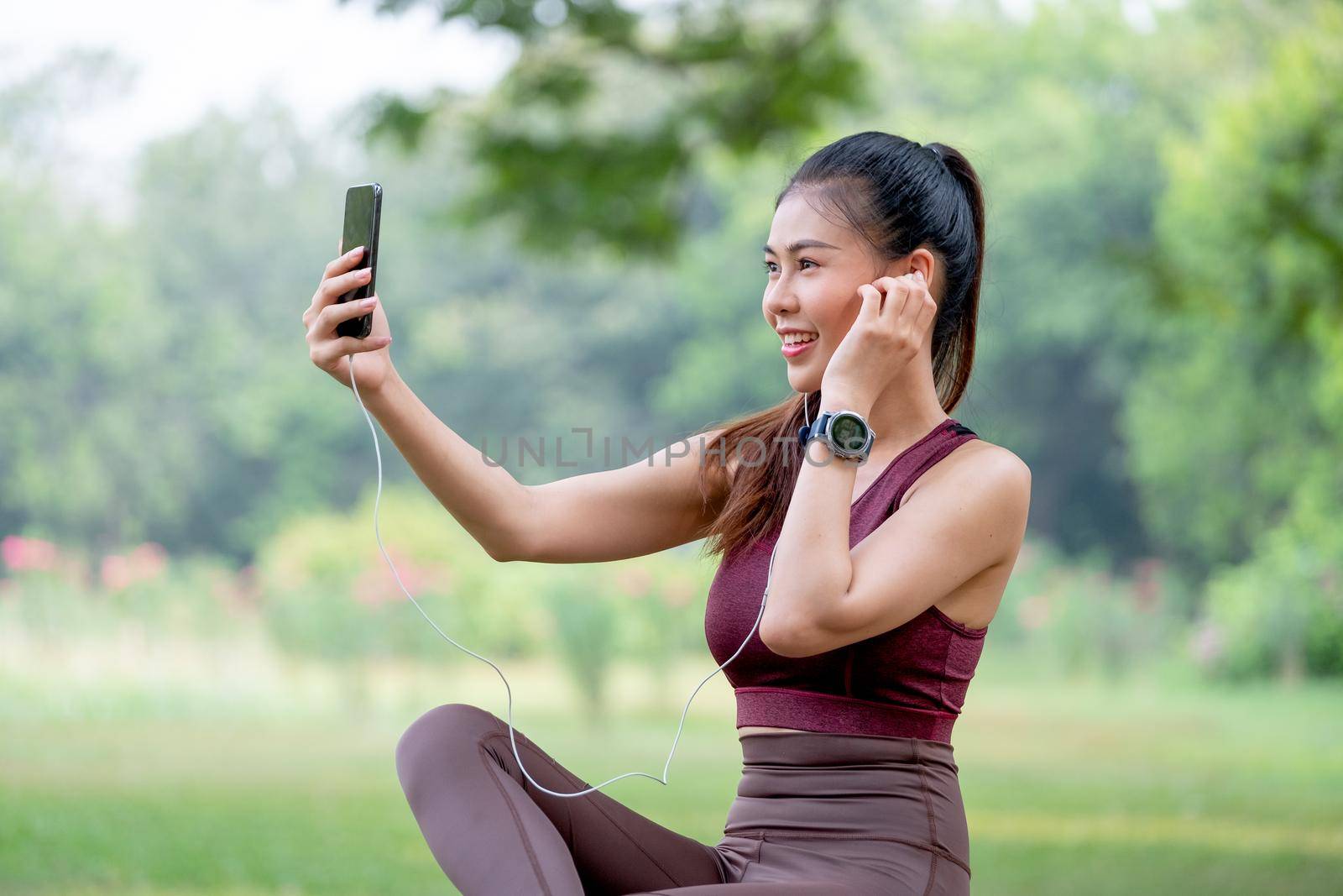 Asian sport woman use mobile phone to selfie during sit in park after exercise in the morning.