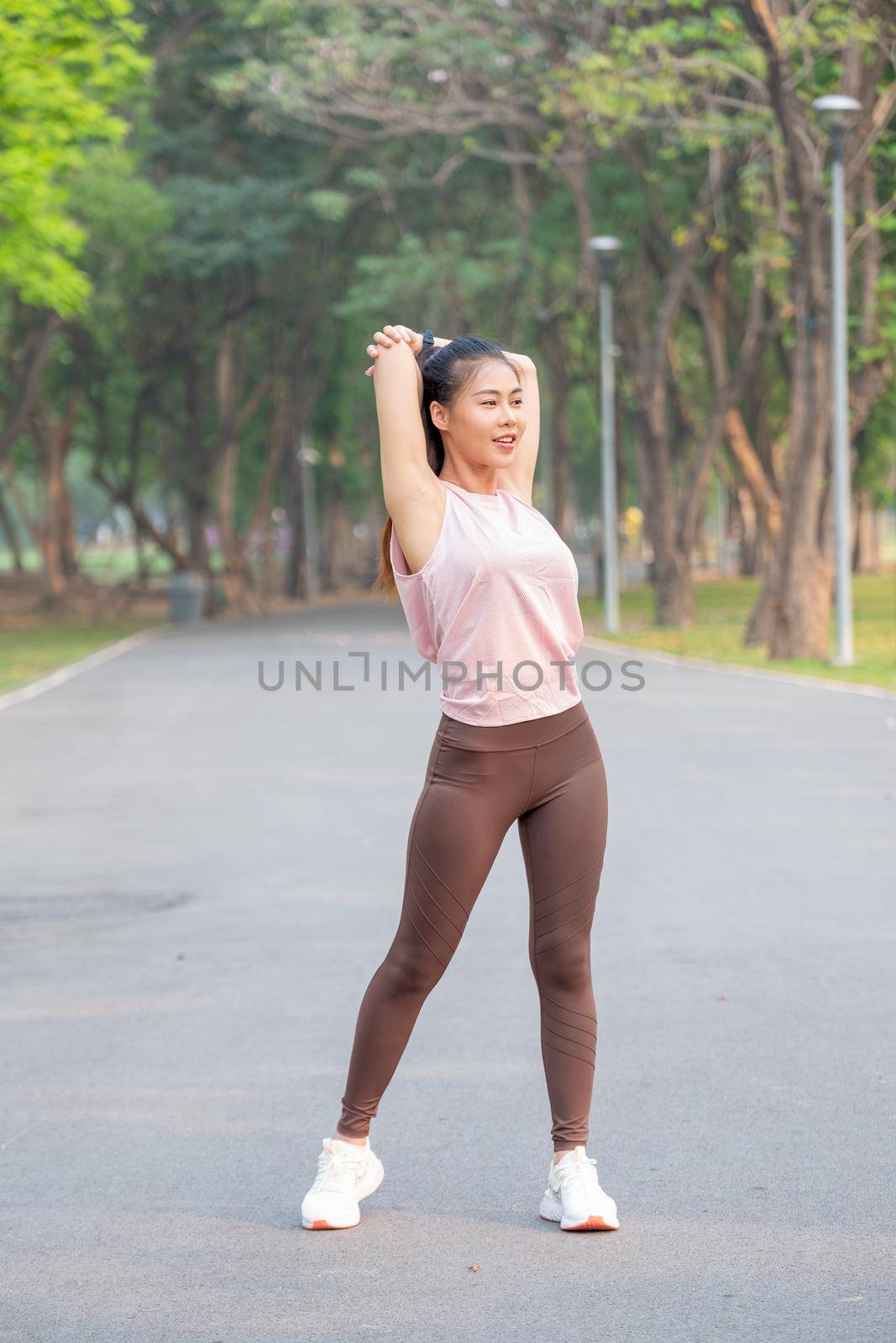 Wide shot and portrait of Asian sport woman do arm and back stretching on road of park during exercise in the morning.
