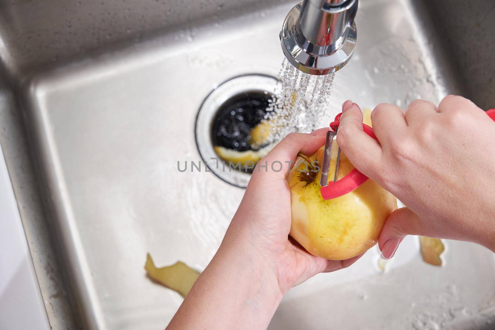 Cropped view of female hands peeling apple over Food waste disposer machine in modern kitchen