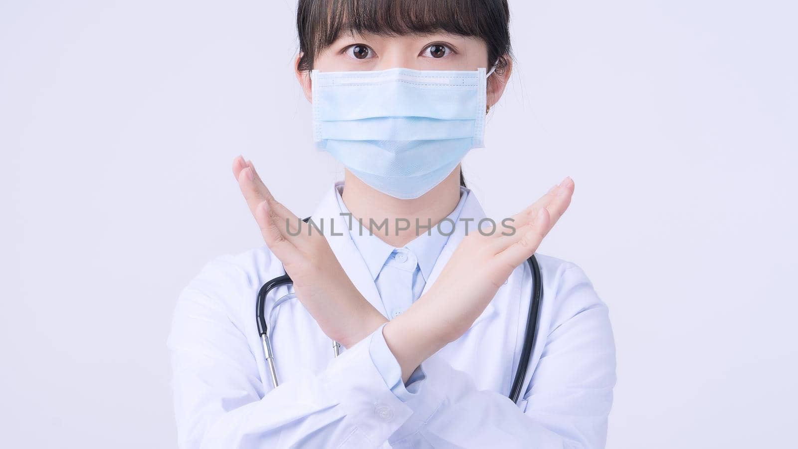 Young female doctor woman wearing mask, making stop sign gesture, saysignaling No isolated on white background, refusing virus disease, close up, blank.