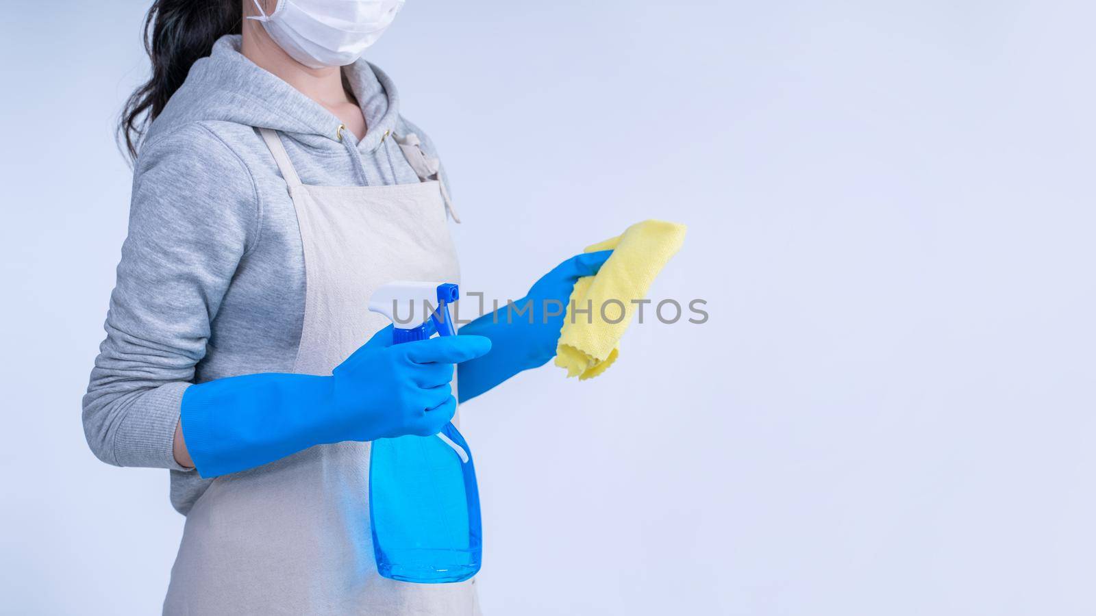 Young woman housekeeper in apron is doing cleaning with blue gloves, wet yellow rag, spraying bottle cleaner, close up, copy space, blank design concept. by ROMIXIMAGE