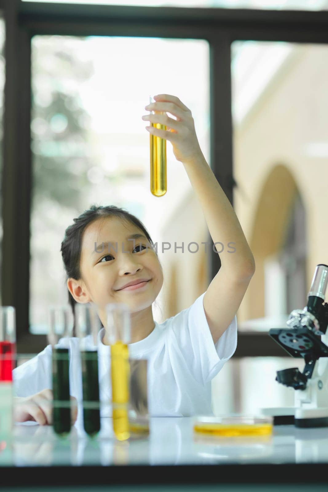 Little girl in lifting and looking at substance in tube in chemistry science class. by ijeab