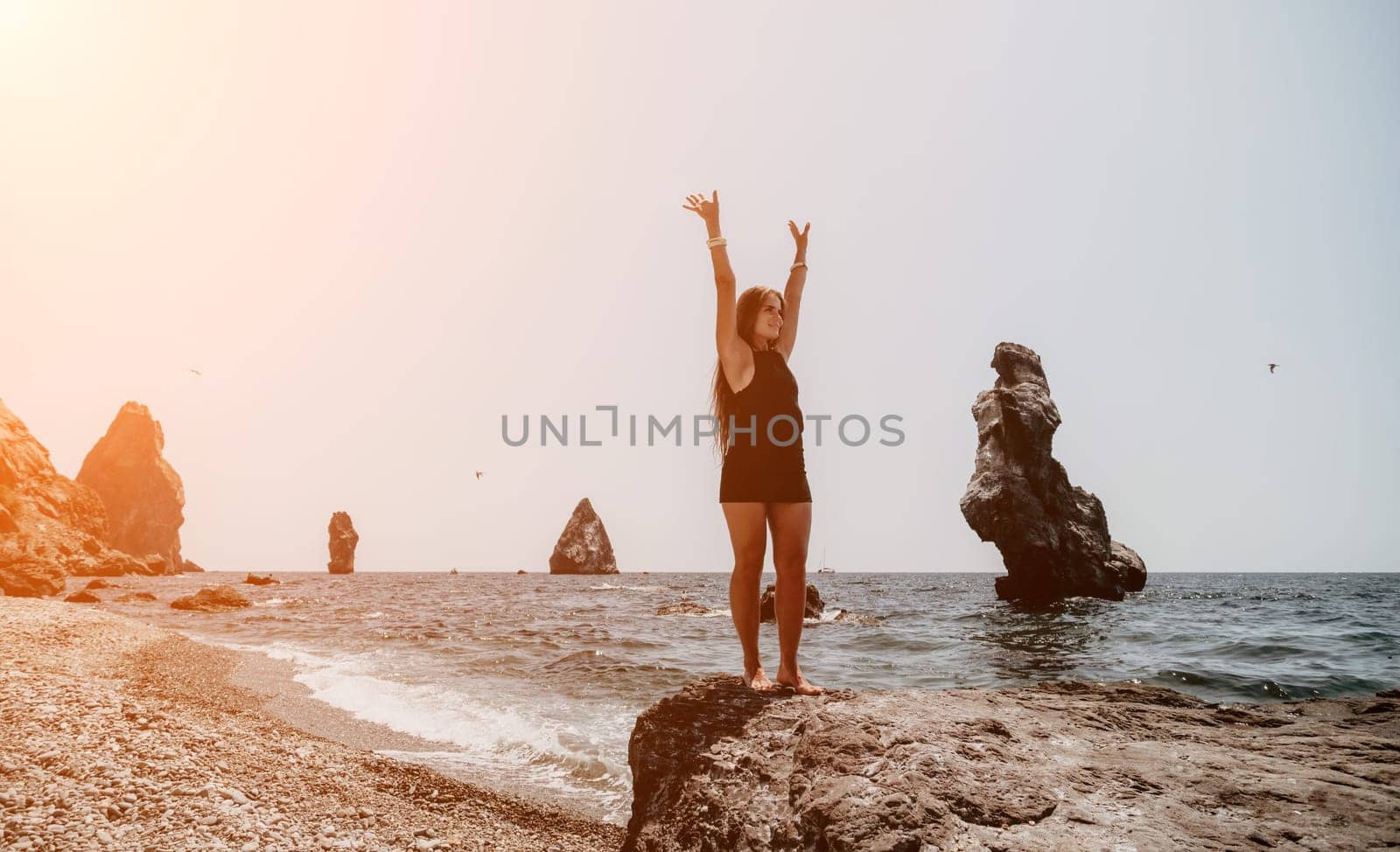 Woman travel sea. Young Happy woman in a long red dress posing on a beach near the sea on background of volcanic rocks, like in Iceland, sharing travel adventure journey