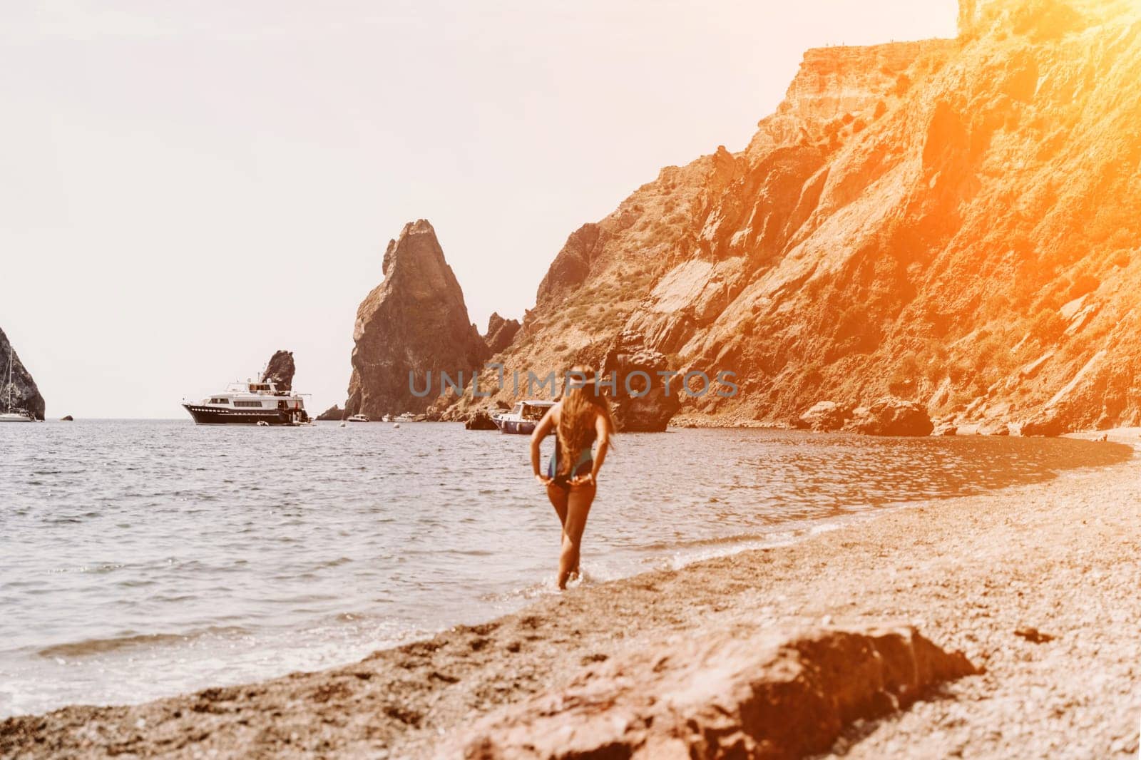 Woman travel summer sea. A happy tourist in a blue bikini enjoying the scenic view of the sea and volcanic mountains while taking pictures to capture the memories of her travel adventure. by Matiunina