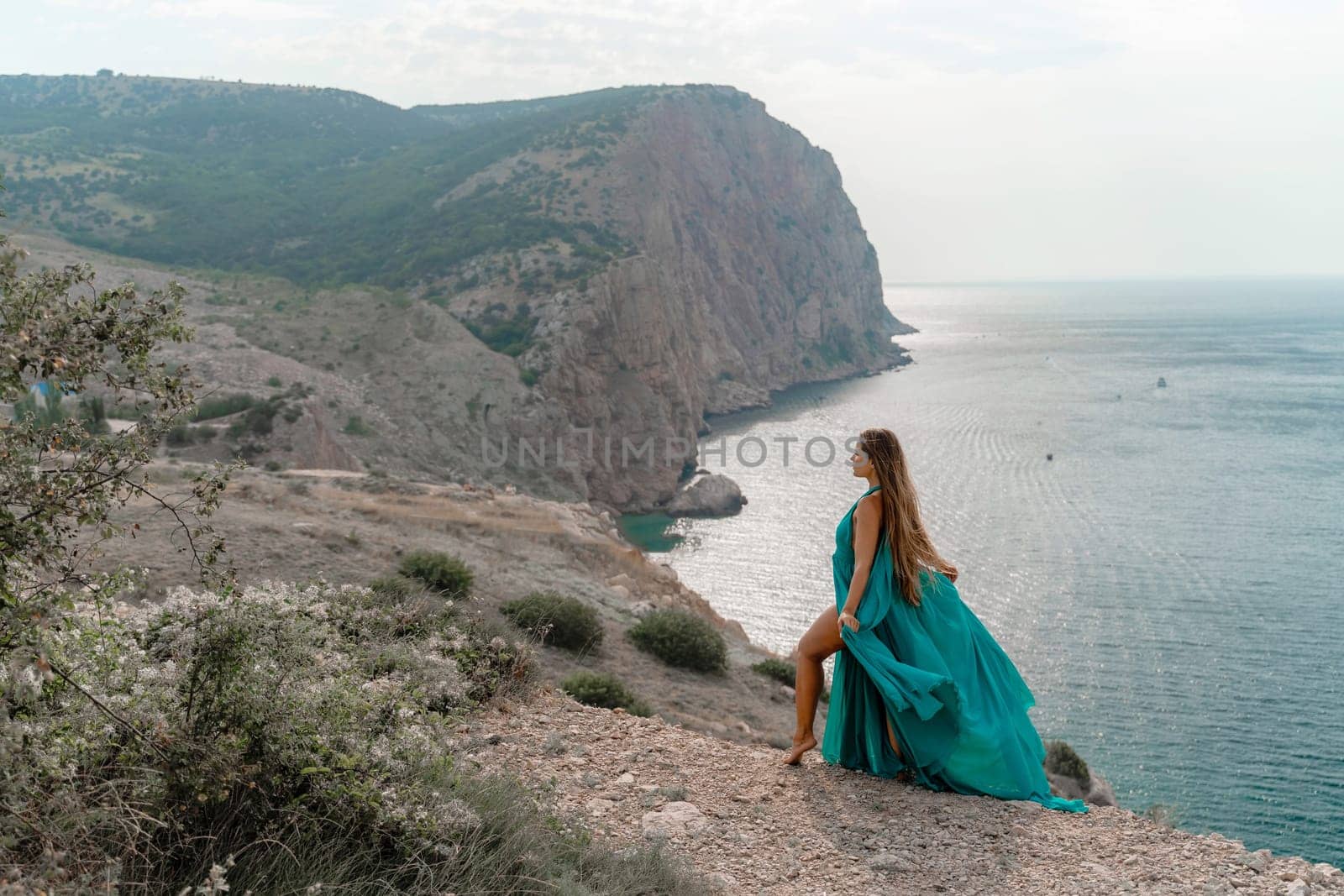 Woman sea trevel green dress. Side view a happy woman with long hair in a long mint dress posing on a beach with calm sea bokeh lights on sunny day. Girl on the nature on blue sky background