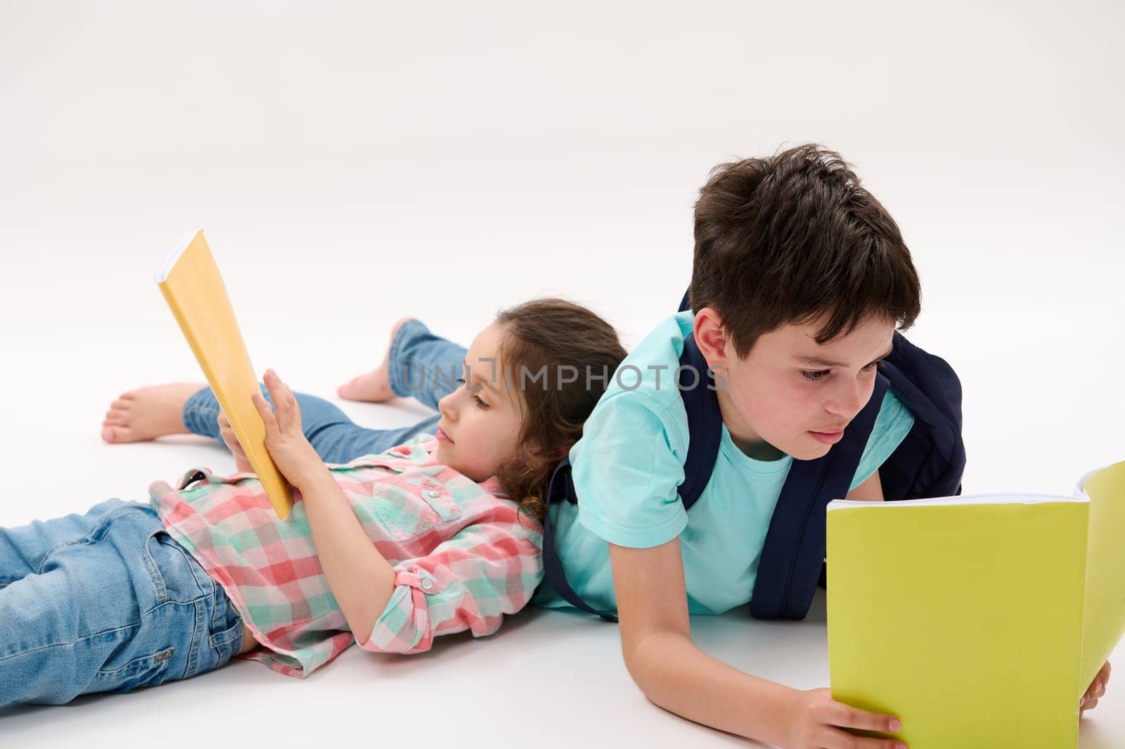 Two smart kids, lovely preschooler girl and teenage boy, brother and sister holding workbooks, doing homework while lying on a white background. Back to school concept. Children Childhood Education