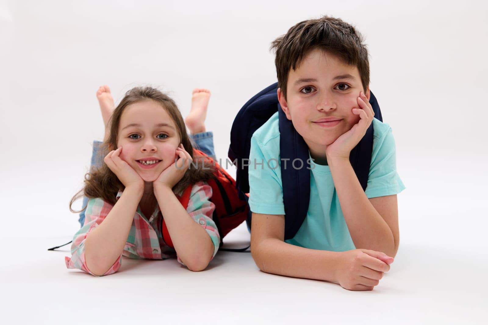 Smart school children, first grader - Caucasian little kid girl 6 years old and Hispanic teenage boy, lying on belly, smiling looking at camera, isolated on white background. Back to school concept