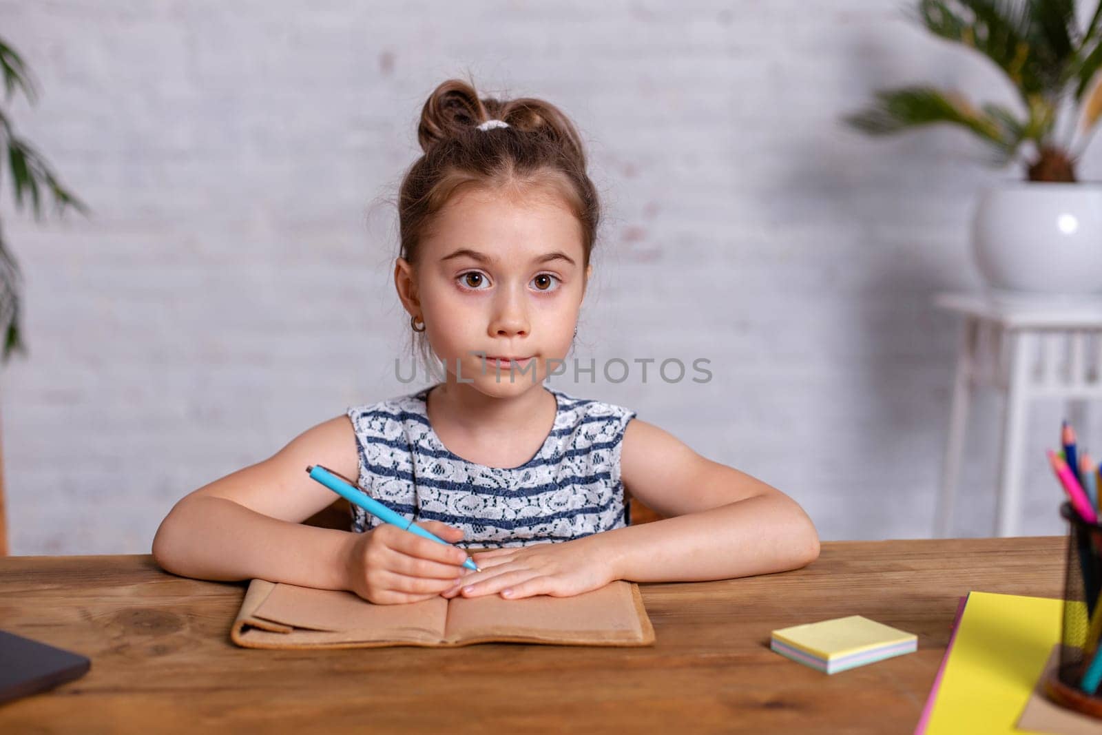 A child girl doing homework writing and reading at home. Little girl writes in a notebook sitting at the table