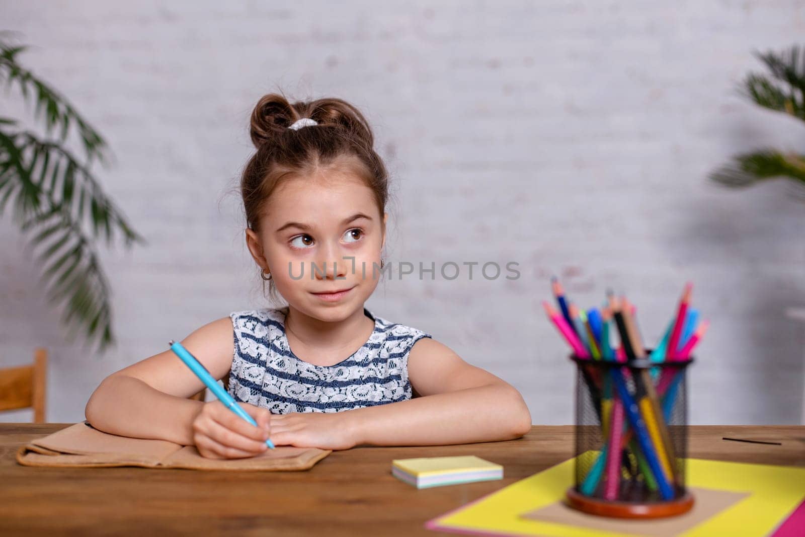 Inspired little girl at the table draw with crayons or do home work by nazarovsergey