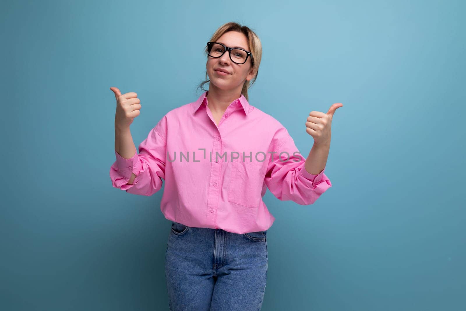 european young blond businesswoman in a pink shirt and jeans is actively gesturing on a studio background with copy space.