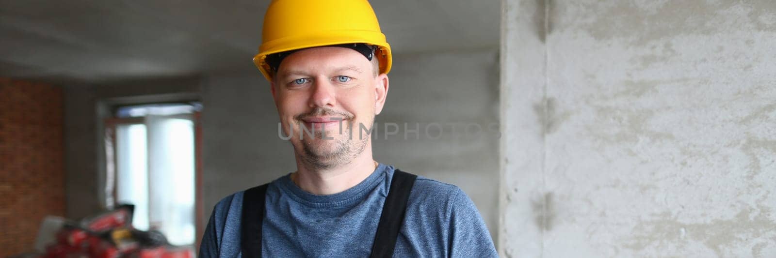 Joyful handyman, builder in uniform and hard hat looks at camera and takes notes on clipboard. Builder foreman preparing for repair work